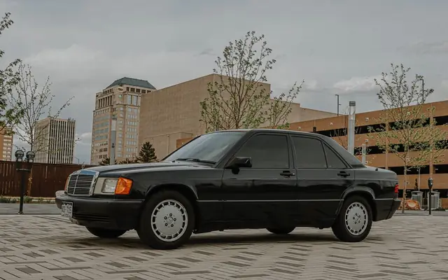 Black Mercedes luxury car parked outdoors in urban area with modern buildings.
