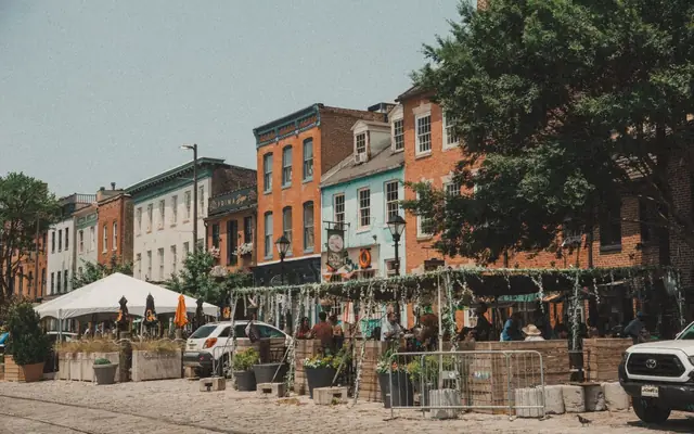 Vibrant street scene in Baltimore with colorful row houses, outdoor cafes, and bustling summer atmosphere.