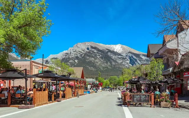 Lively street in Banff, Alberta with outdoor cafes and stunning mountain views, perfect for travel enthusiasts.