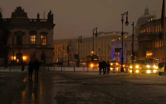 A winter evening street scene in Berlin with illuminated buildings and pedestrians.