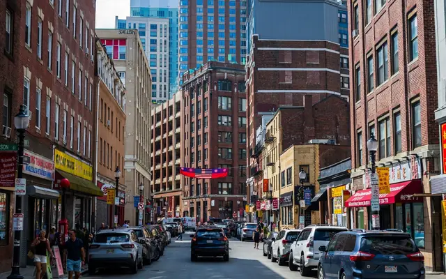 Vibrant street in Boston's Chinatown with cars and pedestrians, showcasing urban life.