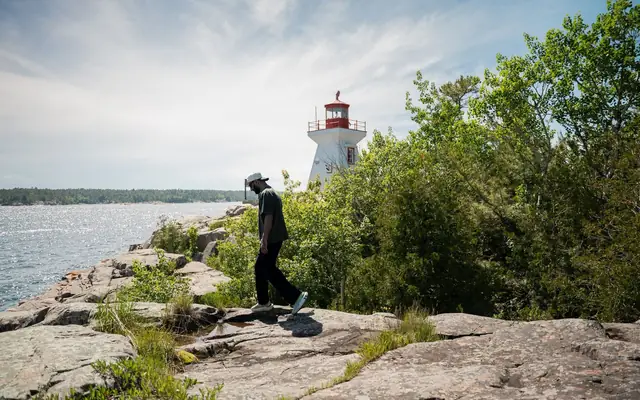 Person walking by a lighthouse on rocky shores in Killarney, Ontario, Canada. Sunny day by the lake.