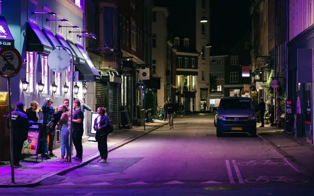 Explore Copenhagen's vibrant nightlife with people enjoying the city streets under purple lights.