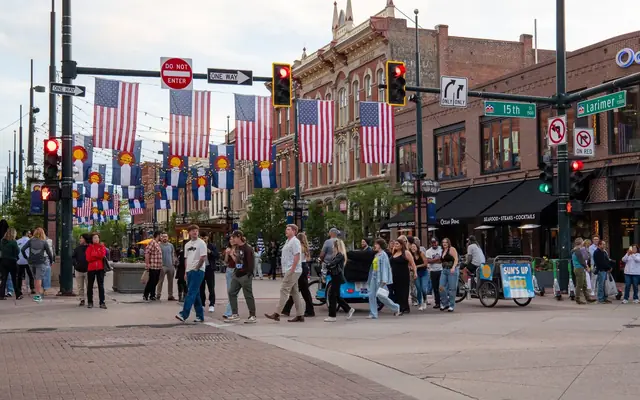People crossing a lively intersection adorned with flags in downtown Denver.