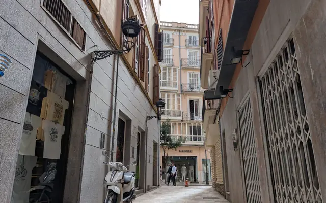 Picturesque alleyway in Ibiza with scooter and people, showcasing traditional Spanish architecture.