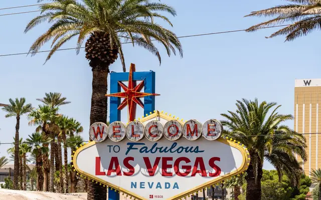 The classic 'Welcome to Las Vegas' sign amidst palm trees, under a bright blue sky.