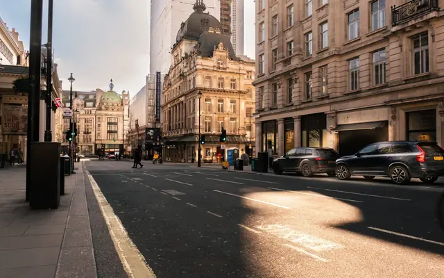 A sunlit street in London's historic district, showcasing Victorian architecture and modern vehicles.