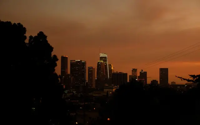 Cityscape of Los Angeles skyscrapers silhouetted against a vibrant orange sunset sky.