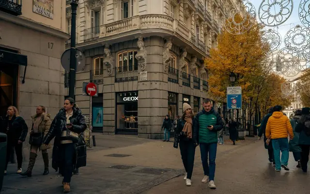 Street scene in Madrid's Calle del Arenal with autumn trees, shoppers, and European architecture.