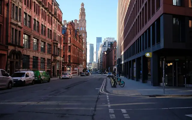 Urban streetscape in Manchester, showcasing modern and historic architecture under a clear blue sky.