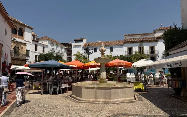 Sunny day in Marbella's picturesque plaza featuring a central fountain and outdoor cafes.