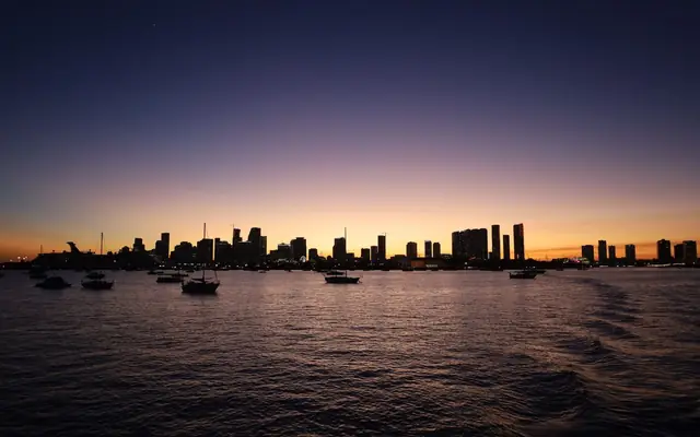 Silhouette of Miami skyline at twilight with boats on the water.