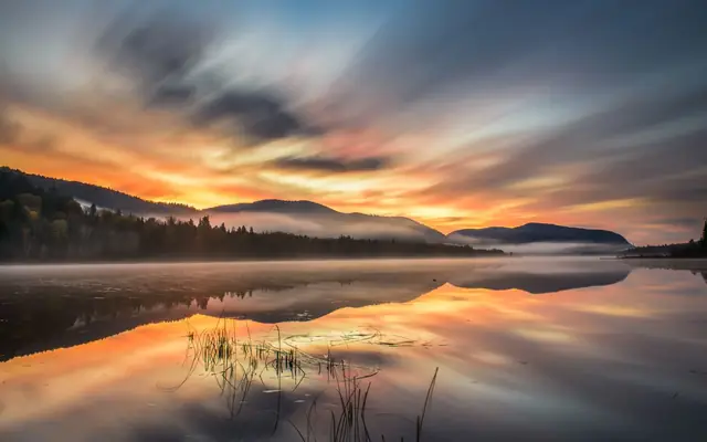 Experience the serene beauty of Mont-Tremblant with this stunning autumn sunrise, reflecting vibrant hues on a calm lake.