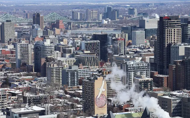 Panoramic winter view of Montreal's skyline with snowy rooftops and iconic Jacques Cartier Bridge.