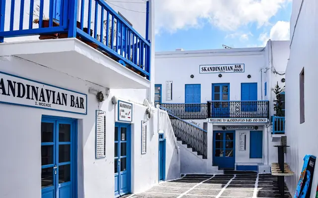 Picturesque Greek alleyway with blue doors and a Scandinavian bar in Mykonos.