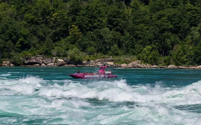Vibrant pink jet boat navigating the rapids of the Niagara River surrounded by lush greenery.