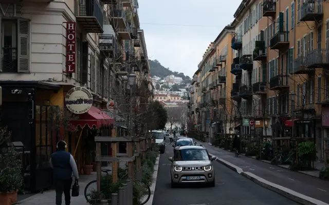 Quaint street view in Nice, France with buildings, cars, and pedestrians.
