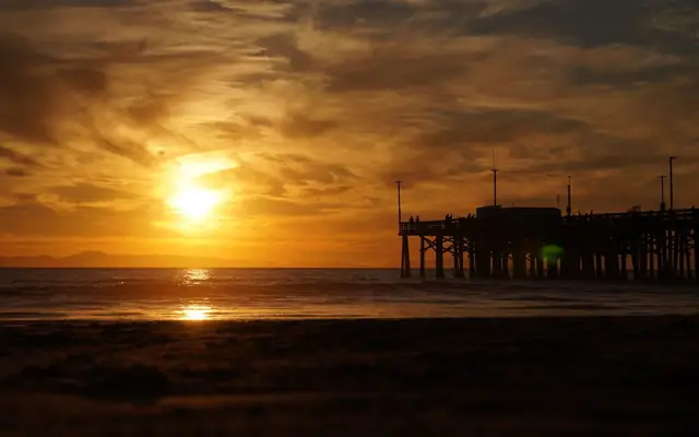 Golden sunset over Newport Beach pier with crashing waves and a vibrant sky.