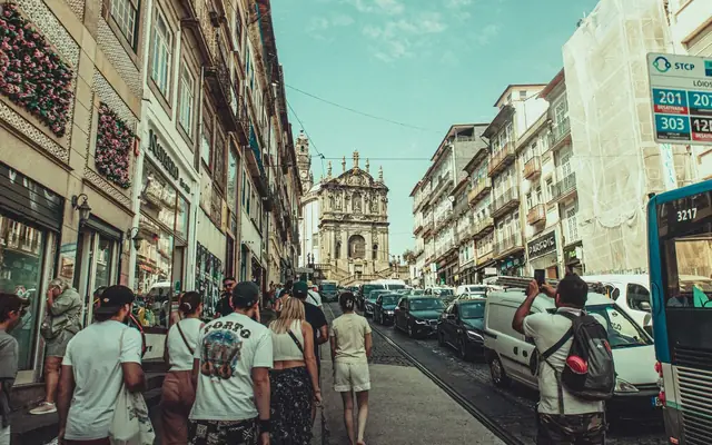 A bustling street in Porto filled with tourists and classic architecture under a clear blue sky.