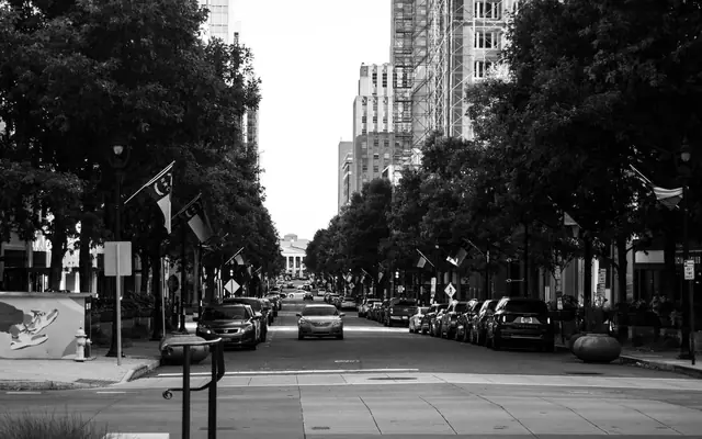 Black and white view of a bustling Raleigh city street with parked cars and flags.