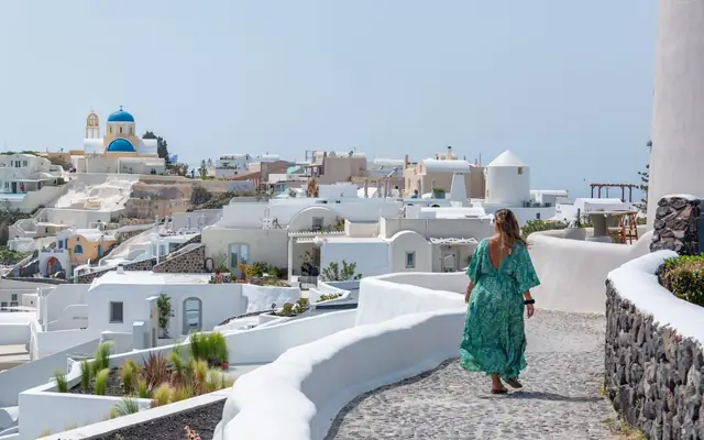 A woman in a green dress walks through the picturesque white buildings of Santorini.