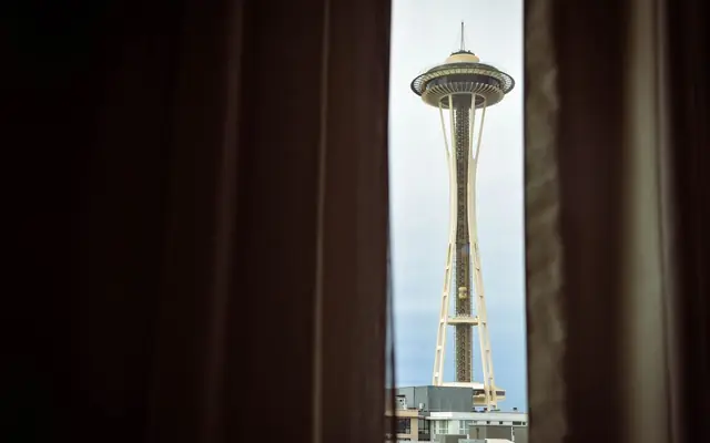 View of Seattle's Space Needle framed by curtains, showcasing iconic architecture.