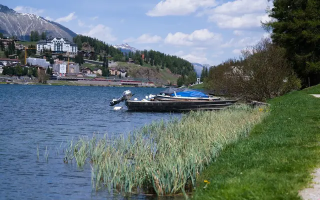 Beautiful landscape of Lake St. Moritz, showcasing boats by the shore with snow-capped mountains in the background.