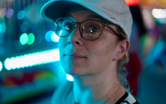 A thoughtful person at a vibrant night fair in Tampa, FL with colorful bokeh.