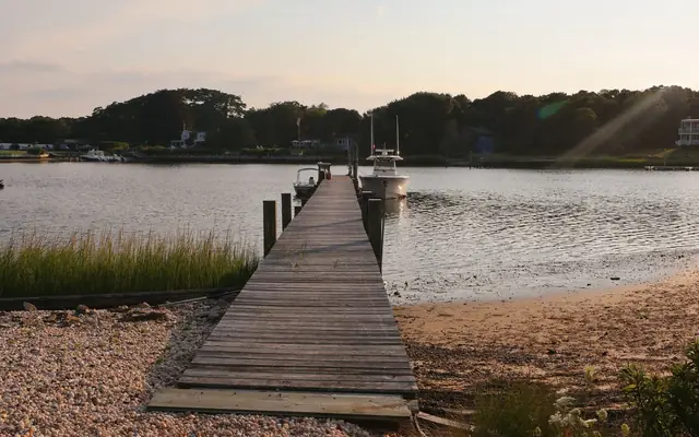 Serene wooden pier at sunset in Hampton Bays, NY, leading to calm waters.