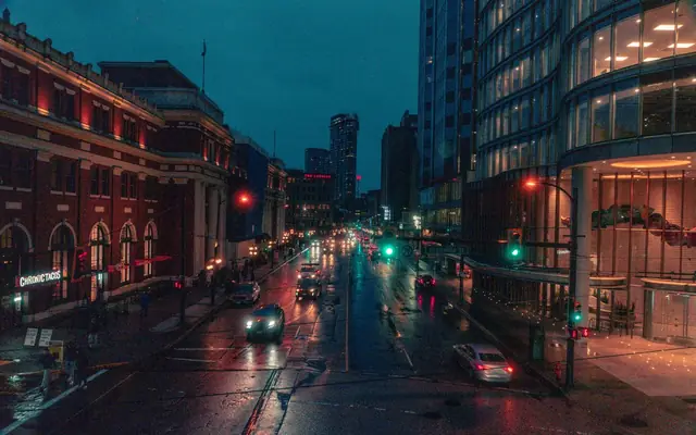 Moody cityscape of a rainy night in downtown Vancouver, capturing illuminated streets and busy urban life.