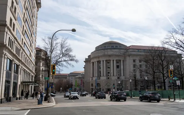 Traffic and pedestrians on a street with historic architecture in Washington DC on a clear day.