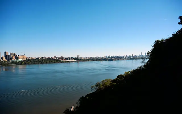 Scenic view of New York City skyline across a tranquil river under a clear blue sky.